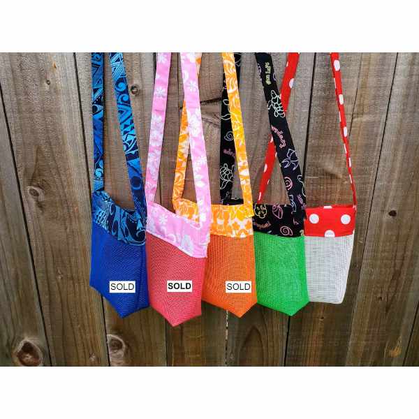 Five colorful mesh beach handbags hanging on a wooden fence, with 'SOLD' labels on each.